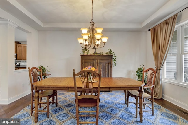 dining space featuring a tray ceiling, visible vents, a chandelier, dark wood-style flooring, and baseboards