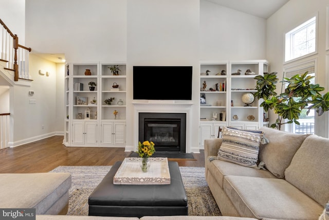 living area featuring a fireplace with flush hearth, a high ceiling, wood finished floors, and baseboards