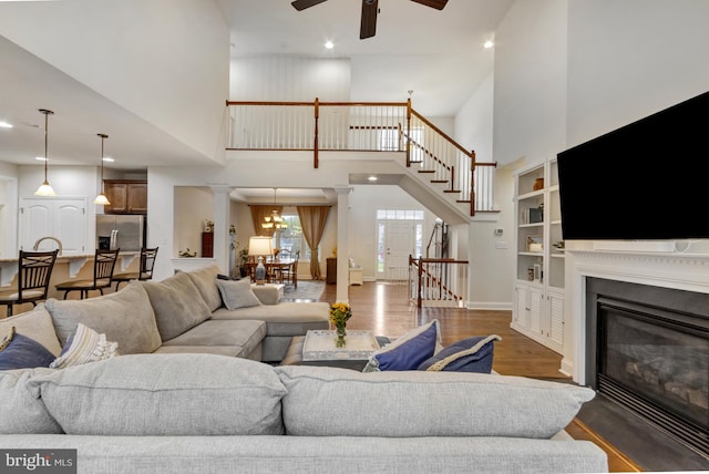 living area with ceiling fan, ornate columns, stairway, a high ceiling, and wood finished floors