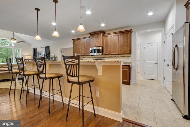 kitchen featuring pendant lighting, a breakfast bar, light stone counters, stainless steel appliances, and brown cabinets