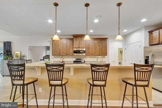 kitchen featuring a sink, stainless steel appliances, backsplash, pendant lighting, and a breakfast bar area