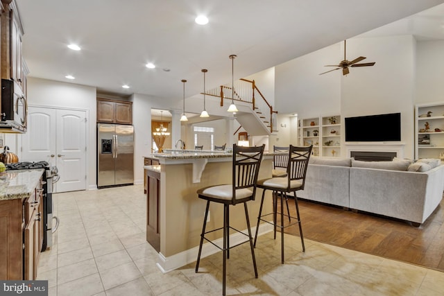 kitchen featuring a breakfast bar, light stone counters, open floor plan, a ceiling fan, and appliances with stainless steel finishes