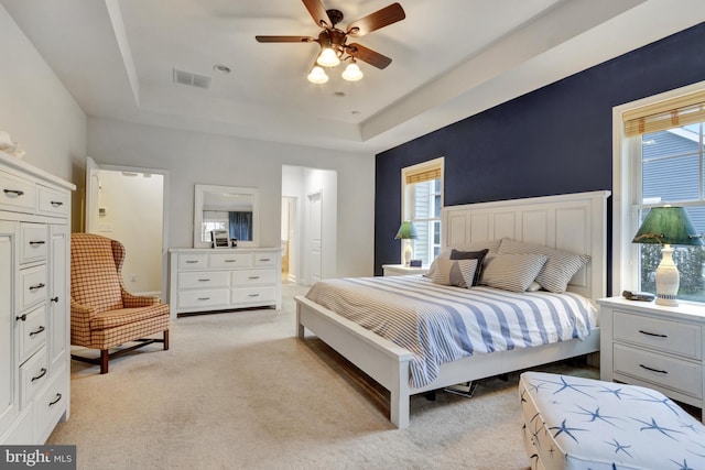 bedroom featuring light carpet, visible vents, multiple windows, and a raised ceiling