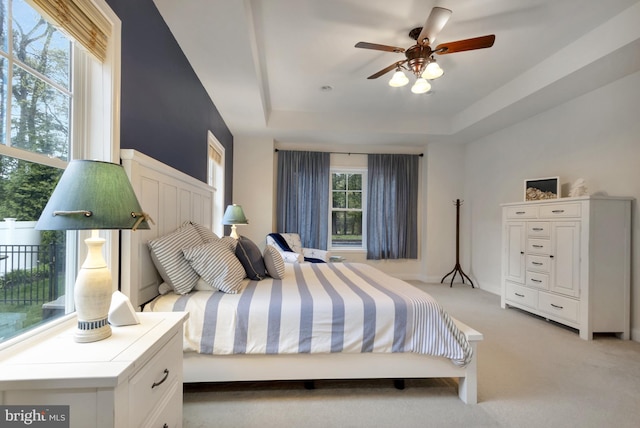 bedroom with light carpet, a tray ceiling, and a ceiling fan