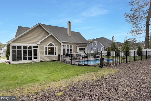back of property with a sunroom, a yard, fence, a chimney, and a fenced in pool