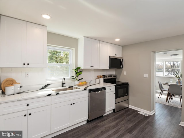 kitchen featuring tasteful backsplash, a sink, appliances with stainless steel finishes, white cabinets, and dark wood-style flooring