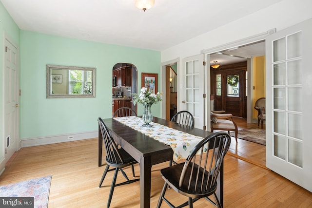 dining room with arched walkways, baseboards, french doors, and light wood finished floors
