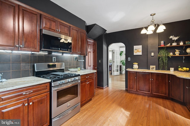 kitchen with a notable chandelier, light wood finished floors, arched walkways, stainless steel appliances, and backsplash