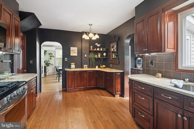 kitchen featuring stainless steel range with gas cooktop, arched walkways, light wood finished floors, and tasteful backsplash
