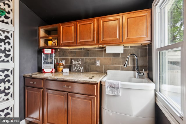 interior space with open shelves, light stone counters, tasteful backsplash, and brown cabinetry