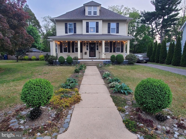 view of front facade with a porch, fence, a shingled roof, and a front lawn