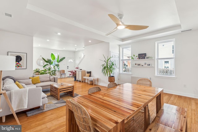 dining room with light wood-style floors, a raised ceiling, a ceiling fan, and visible vents