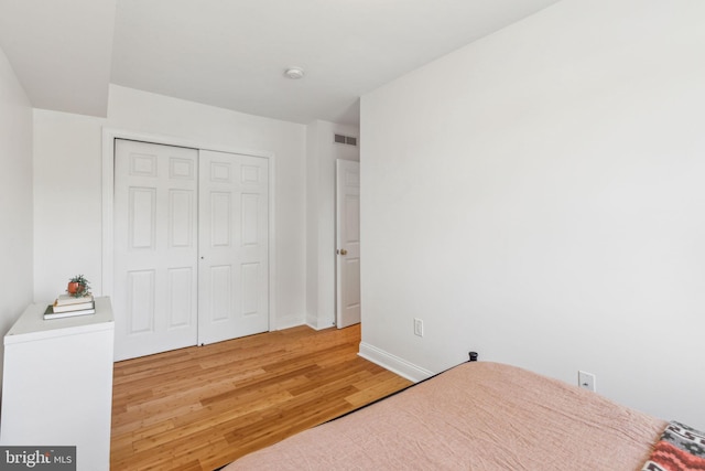unfurnished bedroom with a closet, baseboards, visible vents, and light wood-style floors
