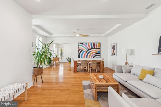 living area with a ceiling fan, visible vents, light wood finished floors, and a raised ceiling