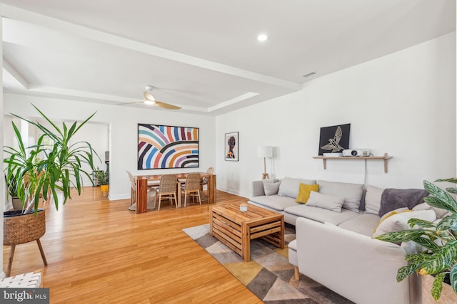 living area with light wood-style floors, baseboards, ceiling fan, recessed lighting, and a tray ceiling