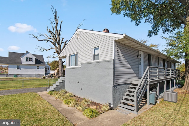 view of property exterior featuring stairs, brick siding, central AC unit, fence, and a lawn