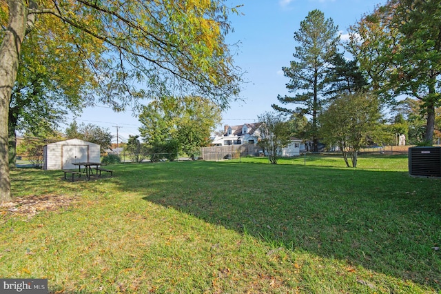 view of yard featuring a storage shed, fence, an outdoor structure, and central air condition unit