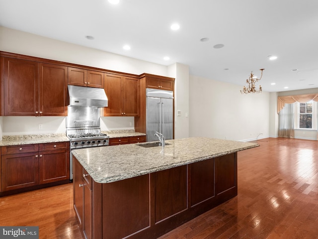 kitchen with an island with sink, premium appliances, under cabinet range hood, a sink, and light stone countertops