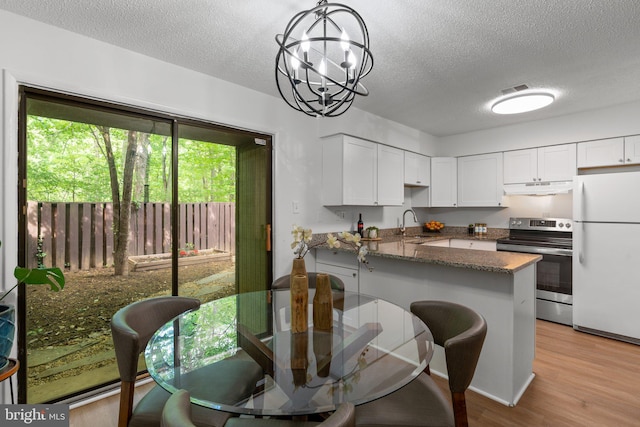 kitchen featuring a textured ceiling, freestanding refrigerator, a peninsula, under cabinet range hood, and stainless steel electric stove