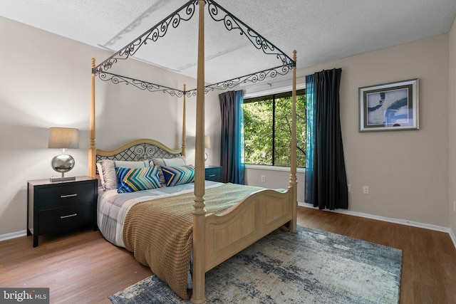 bedroom with baseboards, a textured ceiling, and wood finished floors