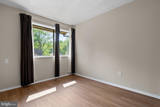 unfurnished room with baseboards, a textured ceiling, visible vents, and wood finished floors