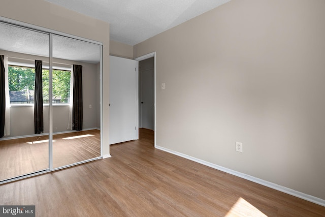 unfurnished bedroom featuring baseboards, wood finished floors, and a closet