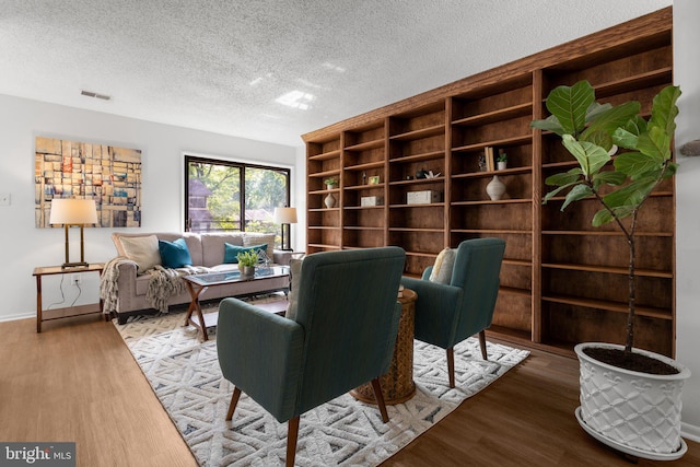 living area with visible vents, a textured ceiling, and wood finished floors