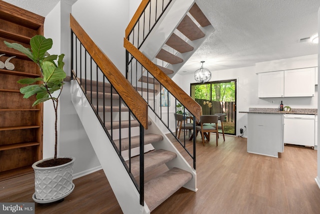 stairway featuring a textured ceiling, visible vents, wood finished floors, baseboards, and a notable chandelier