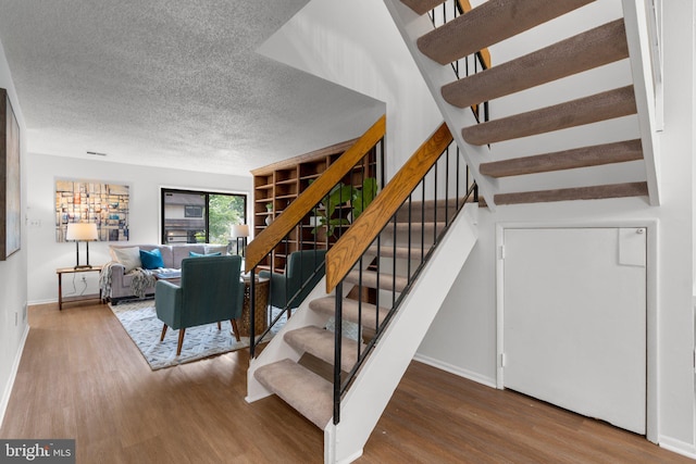 stairway with baseboards, a textured ceiling, wood finished floors, and visible vents