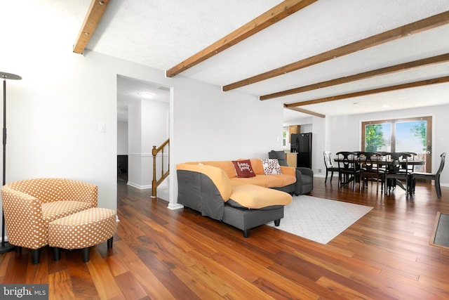 living area with baseboards, wood finished floors, beam ceiling, and stairway