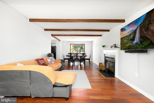 living area featuring baseboards, a fireplace with flush hearth, wood finished floors, and beam ceiling