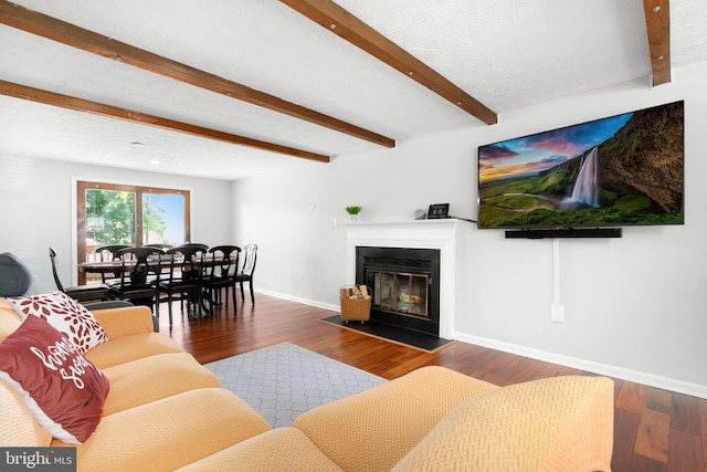 living area with wood finished floors, baseboards, a glass covered fireplace, and beam ceiling