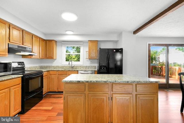 kitchen with a kitchen island, a sink, black appliances, light wood-style floors, and under cabinet range hood