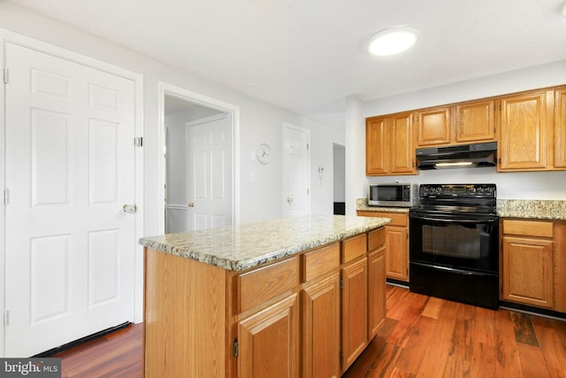 kitchen with a kitchen island, stainless steel microwave, dark wood-style floors, under cabinet range hood, and black range with electric cooktop