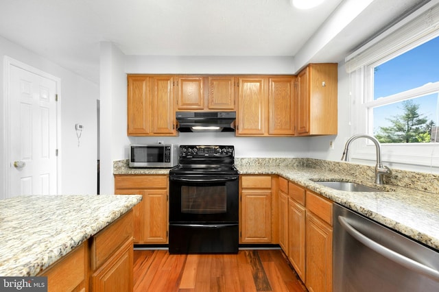 kitchen with light stone counters, a sink, stainless steel appliances, under cabinet range hood, and dark wood-style floors
