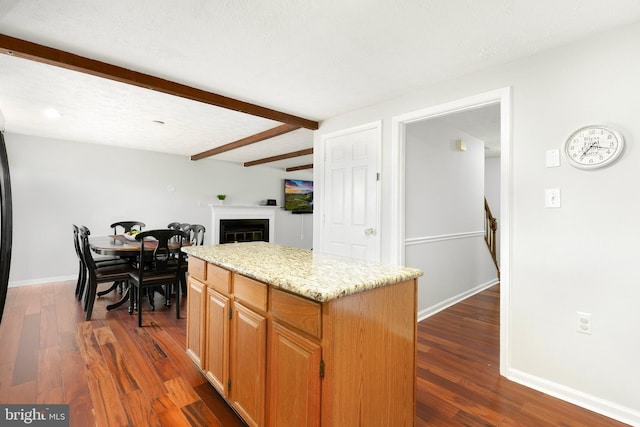 kitchen with a kitchen island, a fireplace, dark wood finished floors, baseboards, and beamed ceiling
