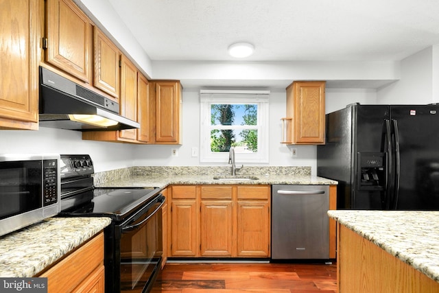 kitchen with dark wood-style flooring, under cabinet range hood, light stone counters, a sink, and black appliances