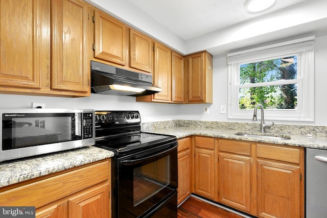 kitchen with dark wood-style floors, under cabinet range hood, light stone counters, a sink, and appliances with stainless steel finishes