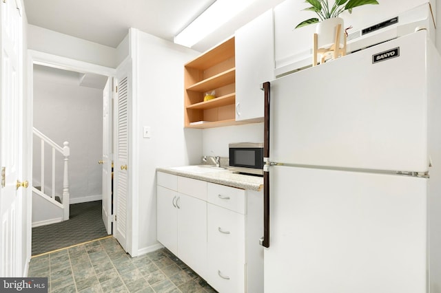 kitchen with open shelves, a sink, white cabinets, freestanding refrigerator, and stainless steel microwave