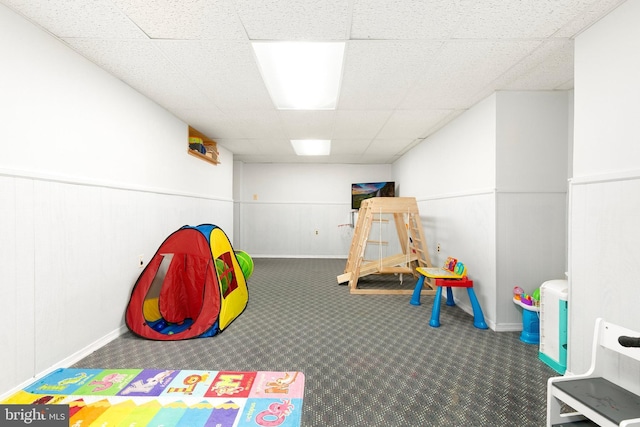 playroom with carpet flooring, baseboards, a paneled ceiling, and a wainscoted wall