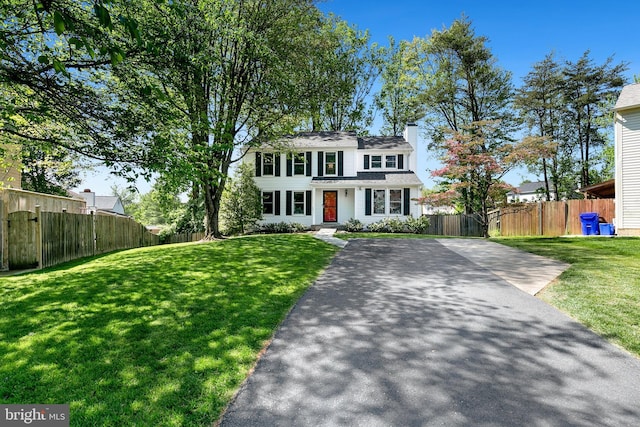 colonial-style house featuring a chimney, fence, and a front yard