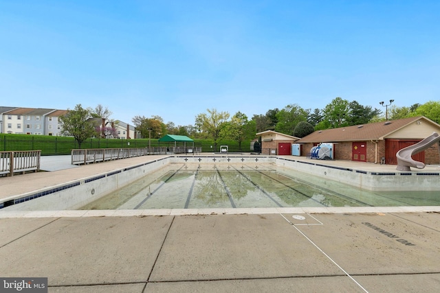 community pool featuring fence and a water slide