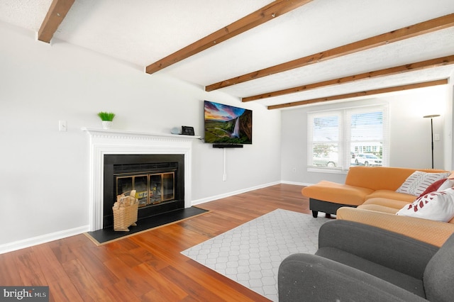 living room featuring a fireplace with flush hearth, baseboards, beam ceiling, and wood finished floors