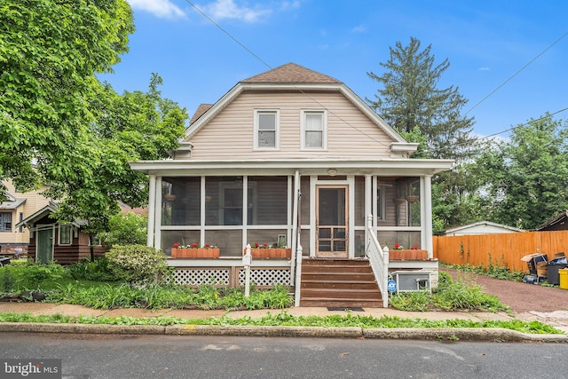 view of front of house featuring a sunroom, fence, and roof with shingles