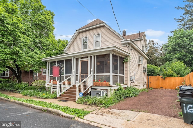 view of front of home with a sunroom, fence, a chimney, and a shingled roof
