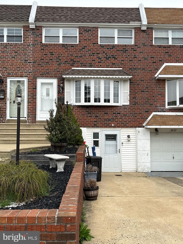 multi unit property featuring roof with shingles, a garage, and brick siding