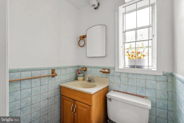 half bathroom featuring tile walls, a wainscoted wall, toilet, and vanity