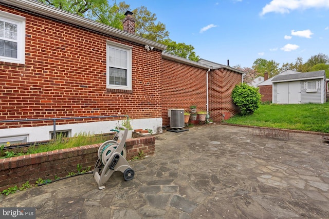 exterior space with an outdoor structure, a patio, a chimney, central AC unit, and brick siding