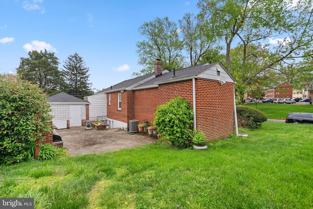 back of house featuring a chimney, brick siding, an outbuilding, a patio, and a lawn