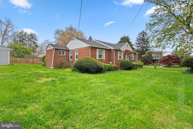 view of side of home featuring a lawn, fence, a chimney, and brick siding